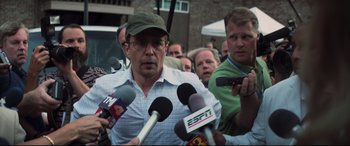 Movie still from “Richard Jewell” (2019), directed by Clint Eastwood – A group of people holding microphones in front of a man; Medium shot, Over the shoulder angle