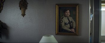 Movie still from “Richard Jewell” (2019), directed by Clint Eastwood – A portrait of a man in uniform hanging on the wall; Medium shot, Over the shoulder angle