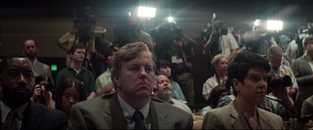 Movie still from “Richard Jewell” (2019), directed by Clint Eastwood – A man in a suit and tie in front of a camera; Close Up shot, Over the shoulder angle