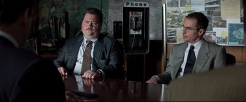 Movie still from “Richard Jewell” (2019), directed by Clint Eastwood – Two men sitting at a table in front of a phone booth; Medium shot, Low angle