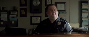 Movie still from “Richard Jewell” (2019), directed by Clint Eastwood – A police officer sitting at a desk in front of a clock; Close Up shot, Low angle