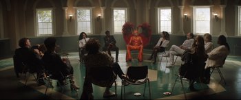 Movie still from “Rocketman” (2019), directed by Dexter Fletcher – A group of people sitting in a circle with a person in an orange suit; Wide shot, High angle