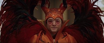 Movie still from “Rocketman” (2019), directed by Dexter Fletcher – A man in a costume with glasses and an orange jacket; Close Up shot, Low angle