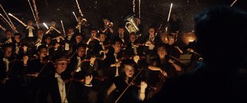 Movie still from “Rocketman” (2019), directed by Dexter Fletcher – A large group of people in black suits holding musical instruments; Extreme Wide shot, Low angle