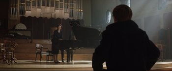 Movie still from “Rocketman” (2019), directed by Dexter Fletcher – A woman sitting in front of a grand piano in a room; Wide shot, Over the shoulder angle