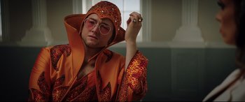 Movie still from “Rocketman” (2019), directed by Dexter Fletcher – A man in a orange outfit and a ring; Medium shot, Low angle