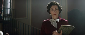 Movie still from “Rocketman” (2019), directed by Dexter Fletcher – An older woman wearing a red jacket and a white bow tie; Medium shot, Low angle