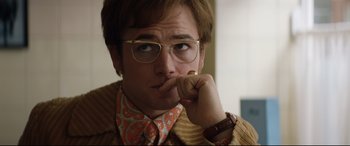 Movie still from “Rocketman” (2019), directed by Dexter Fletcher – A man with glasses is wearing a jacket and a tie; Close Up shot, Over the shoulder angle