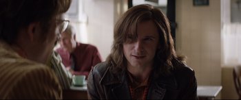 Movie still from “Rocketman” (2019), directed by Dexter Fletcher – A man with long brown hair wearing a leather jacket; Close Up shot, Over the shoulder angle