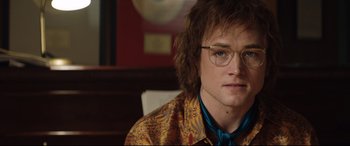 Movie still from “Rocketman” (2019), directed by Dexter Fletcher – A young man wearing glasses sitting in front of a mirror; Close Up shot, Over the shoulder angle