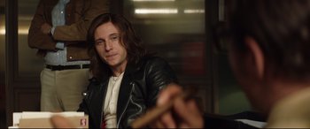 Movie still from “Rocketman” (2019), directed by Dexter Fletcher – A man with long hair and a leather jacket holding a wooden stick; Close Up shot, Over the shoulder angle