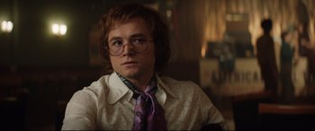 Movie still from “Rocketman” (2019), directed by Dexter Fletcher – A young man wearing glasses and wearing a tie; Close Up shot, Low angle