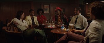Movie still from “Rocketman” (2019), directed by Dexter Fletcher – A group of people sitting at a table drinking and smoking; Wide shot, High angle
