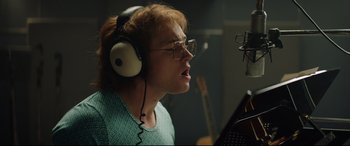 Movie still from “Rocketman” (2019), directed by Dexter Fletcher – A woman with glasses and headphones in a recording studio; Close Up shot, Low angle
