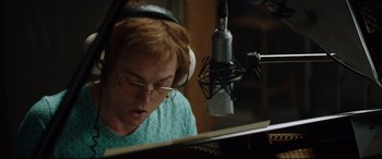 Movie still from “Rocketman” (2019), directed by Dexter Fletcher – A woman with glasses and headphones is sitting at a piano; Close Up shot, Low angle