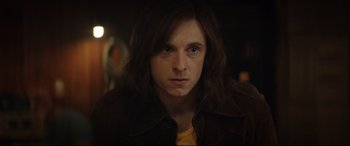 Movie still from “Rocketman” (2019), directed by Dexter Fletcher – A man with long hair is looking at the camera; Close Up shot, Over the shoulder angle