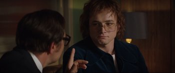 Movie still from “Rocketman” (2019), directed by Dexter Fletcher – A young man in glasses talking to another man; Close Up shot, Over the shoulder angle