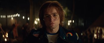 Movie still from “Rocketman” (2019), directed by Dexter Fletcher – A man in a leather jacket with a rainbow on his shirt; Close Up shot, Low angle