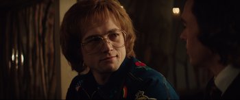 Movie still from “Rocketman” (2019), directed by Dexter Fletcher – A man with red hair wearing glasses and a blue shirt; Close Up shot, Over the shoulder angle