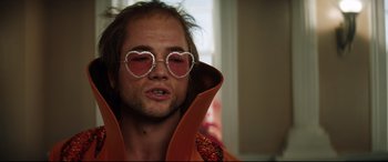 Movie still from “Rocketman” (2019), directed by Dexter Fletcher – A person wearing heart shaped glasses; Close Up shot, Low angle