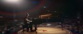 Movie still from “Rocketman” (2019), directed by Dexter Fletcher – A man sitting in front of a grand piano on a stage; Wide shot, High angle