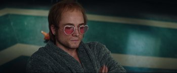 Movie still from “Rocketman” (2019), directed by Dexter Fletcher – A man with red hair wearing heart shaped glasses; Close Up shot, Over the shoulder angle