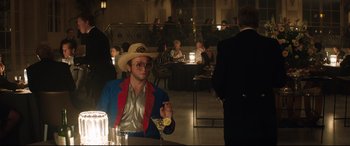 Movie still from “Rocketman” (2019), directed by Dexter Fletcher – A man in a cowboy hat sitting at a table with a drink; Medium shot, Over the shoulder angle