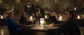 Movie still from “Rocketman” (2019), directed by Dexter Fletcher – A group of diners are sitting around a round table; Wide shot, High angle