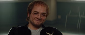 Movie still from “Rocketman” (2019), directed by Dexter Fletcher – A person wearing glasses and a jacket; Close Up shot, Over the shoulder angle