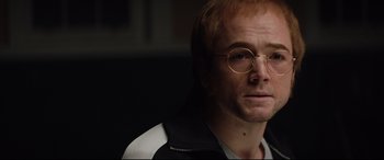 Movie still from “Rocketman” (2019), directed by Dexter Fletcher – A person wearing glasses and a jacket; Close Up shot, Over the shoulder angle