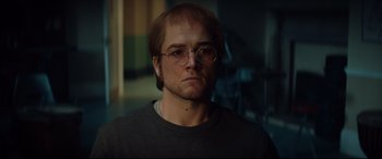 Movie still from “Rocketman” (2019), directed by Dexter Fletcher – A person wearing glasses and a sweater; Close Up shot, Over the shoulder angle