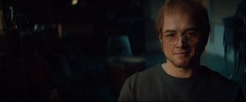 Movie still from “Rocketman” (2019), directed by Dexter Fletcher – A person wearing glasses in a room; Close Up shot, Over the shoulder angle