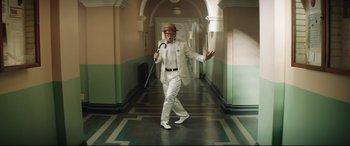 Movie still from “Rocketman” (2019), directed by Dexter Fletcher – An older man in a white suit and hat walking down a hall way; Wide shot, Low angle