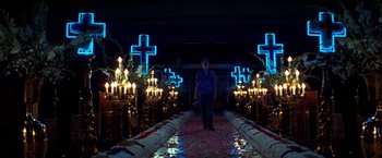 Movie still from “Romeo + Juliet” (1996), directed by Baz Luhrmann – A woman standing in front of candles and crosses in a dark room; Wide shot, Low angle