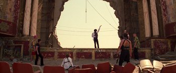 Movie still from “Romeo + Juliet” (1996), directed by Baz Luhrmann – A man standing on top of a stage in front of two other people; Wide shot, Low angle