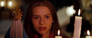 Movie still from “Romeo + Juliet” (1996), directed by Baz Luhrmann – A girl with her hands over her mouth and a candle in the background; Close Up shot, High angle