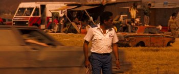 Movie still from “Romeo + Juliet” (1996), directed by Baz Luhrmann – A man walking down the street holding a bag; Medium shot, Over the shoulder angle