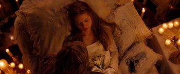 Movie still from “Romeo + Juliet” (1996), directed by Baz Luhrmann – A woman laying in a bed with a man holding a white flower; Close Up shot, High angle