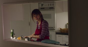 Movie still from “Ruby Sparks” (2012), directed by Valerie Faris – A woman in an apron standing in a kitchen preparing food; Medium shot, Over the shoulder angle