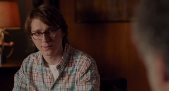 Movie still from “Ruby Sparks” (2012), directed by Valerie Faris – A man sitting in front of a wooden wall wearing glasses; Close Up shot, Over the shoulder angle
