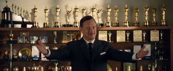 Movie still from “Saving Mr. Banks” (2013), directed by John Lee Hancock – A man in a suit and tie in front of a row of trophies; Medium shot, Low angle