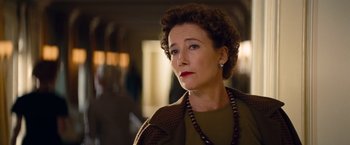 An older woman wearing a brown jacket and a red necklace