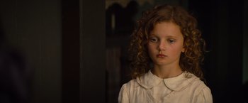 A young girl in a white shirt is looking at the camera