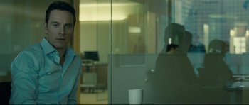 Movie still from “Shame” (2011), directed by Steve McQueen – A man is sitting in front of a glass wall; Medium shot, Over the shoulder angle