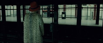 Movie still from “Shame” (2011), directed by Steve McQueen – A woman in a red hat and a leopard print coat looking out a train window; Medium shot, Over the shoulder angle