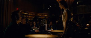Movie still from “Shame” (2011), directed by Steve McQueen – A group of people sitting at tables in a room; Medium shot, Over the shoulder angle