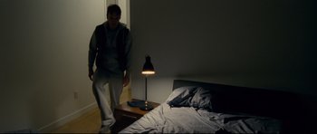 Movie still from “Shame” (2011), directed by Steve McQueen – A man standing next to a nightstand next to a bed; Wide shot, High angle