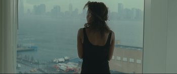 Movie still from “Shame” (2011), directed by Steve McQueen – A woman standing in front of a window looking out at a city; Medium shot, Over the shoulder angle