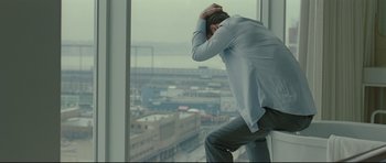 Movie still from “Shame” (2011), directed by Steve McQueen – A man leaning against a window ledge looking out at a city; Medium shot, High angle