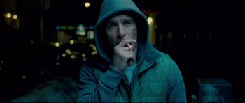 Movie still from “Shame” (2011), directed by Steve McQueen – A man in a hooded jacket is smoking a cigarette; Close Up shot, Low angle